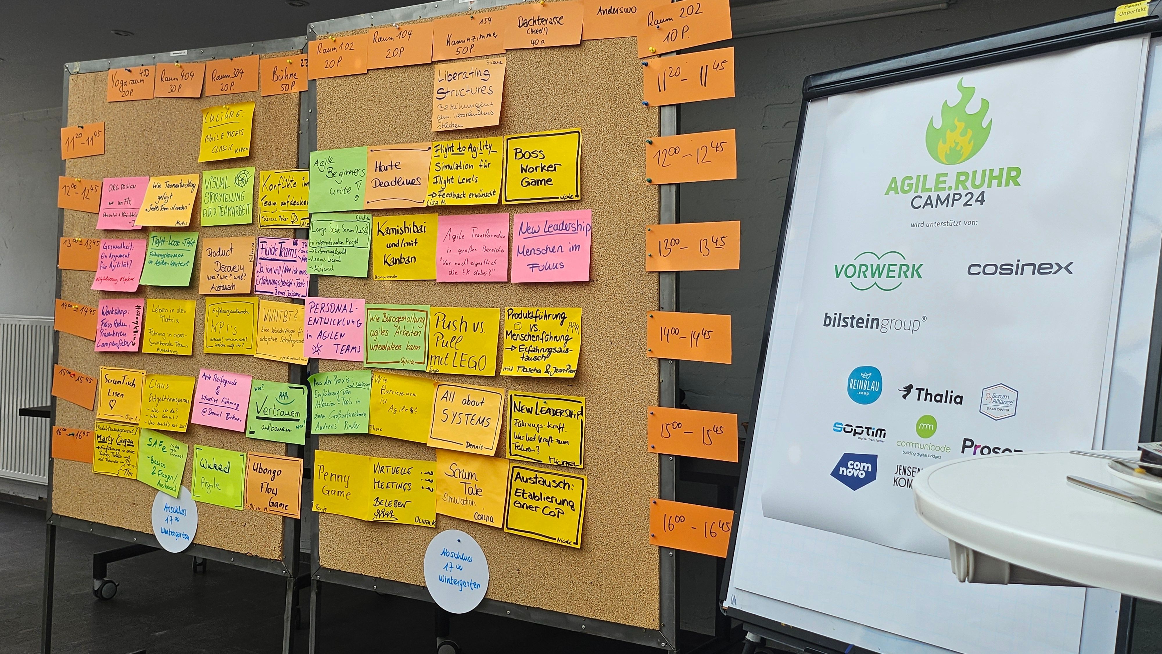 Large pinboard with colored sticky notes for session planning, next to it a roll-up banner with the logo ‘AGILE.RUHR Camp24’ and sponsors